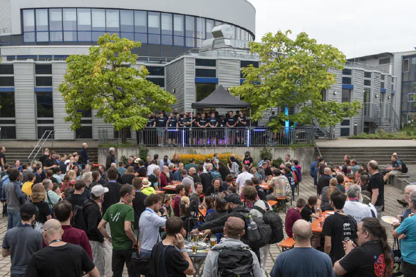 Wide shot of the courtyard at the Social Event, filled with tables, benches and people.